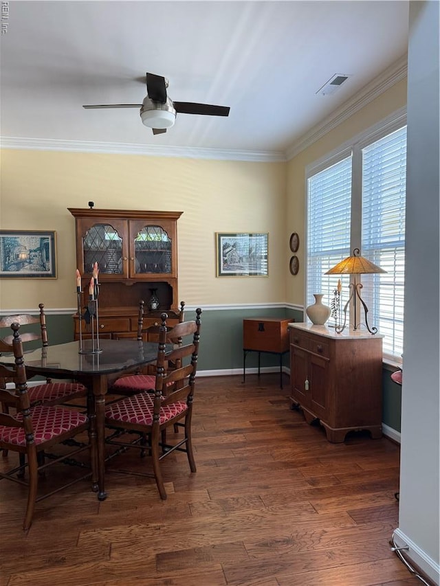 dining room featuring a ceiling fan, visible vents, crown molding, baseboards, and dark wood-style floors