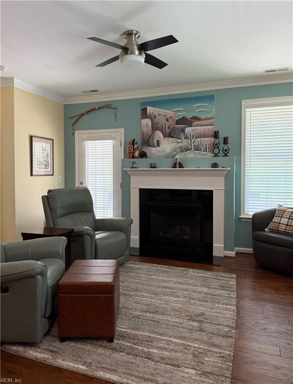 living area featuring visible vents, ornamental molding, wood finished floors, a fireplace, and a ceiling fan