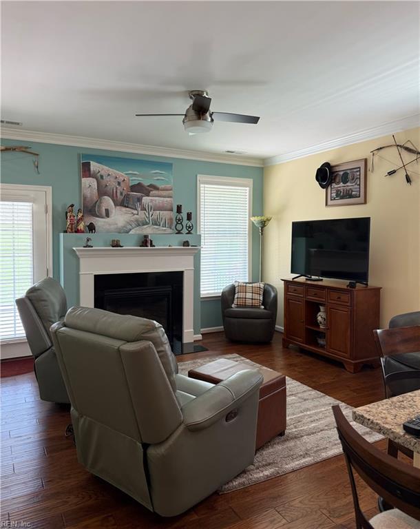 living area with ceiling fan, visible vents, crown molding, a fireplace, and dark wood finished floors