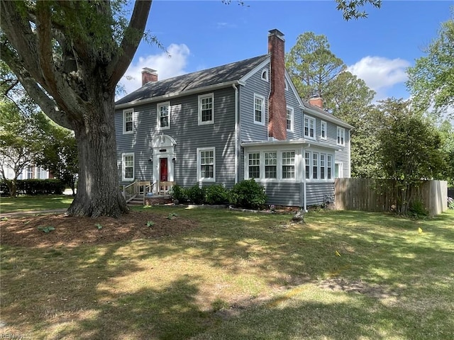 colonial home with fence, a chimney, and a front lawn