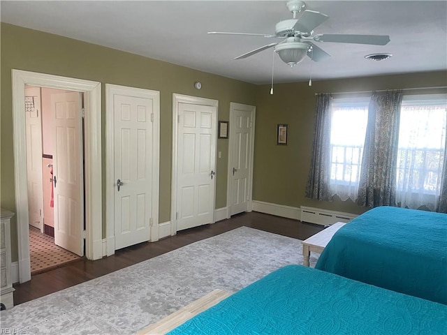 bedroom with visible vents, multiple closets, wood finished floors, baseboards, and a baseboard heating unit