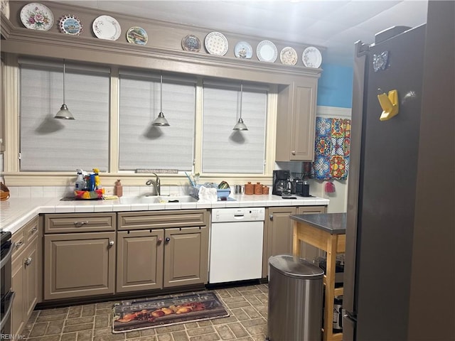 kitchen with tile countertops, stove, dishwasher, a sink, and freestanding refrigerator