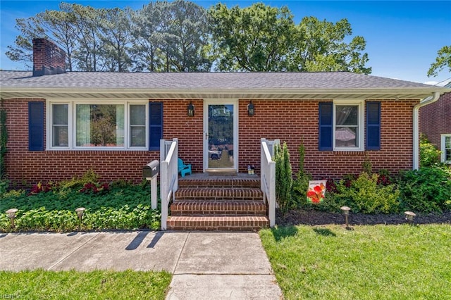 view of front of home with brick siding, a front lawn, and a chimney