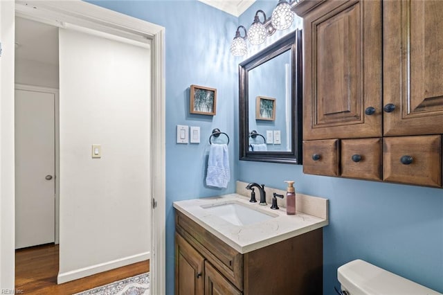 half bathroom featuring vanity, ornamental molding, wood finished floors, toilet, and baseboards