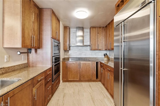 kitchen with brown cabinetry, built in appliances, and wall chimney range hood