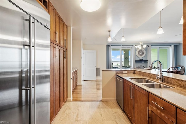 kitchen featuring brown cabinetry, baseboards, a sink, appliances with stainless steel finishes, and hanging light fixtures