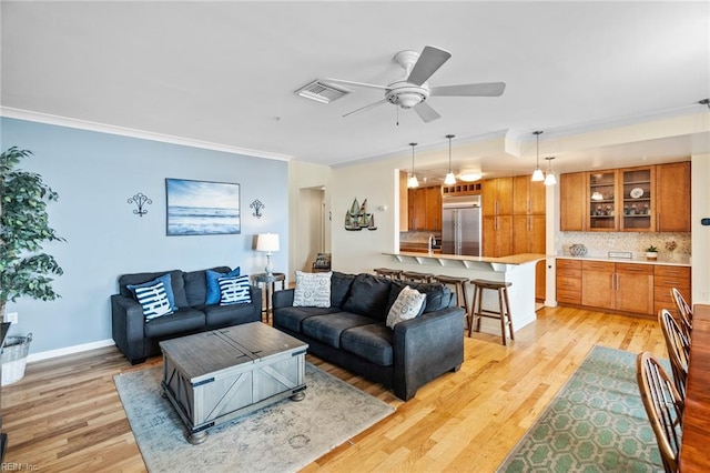 living area with visible vents, ornamental molding, light wood-style floors, and ceiling fan