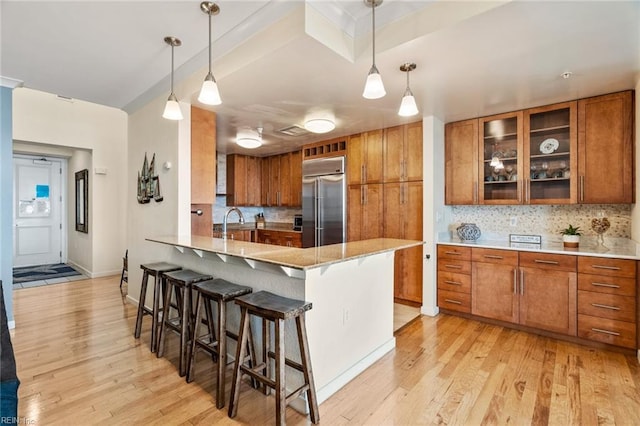 kitchen featuring light wood-style floors, stainless steel built in fridge, brown cabinets, and tasteful backsplash