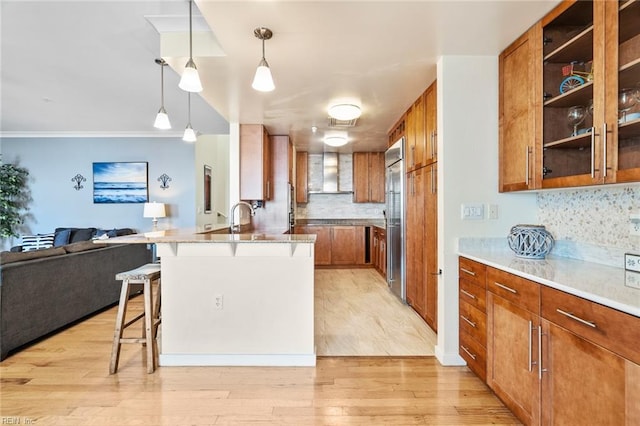 kitchen with brown cabinets, a breakfast bar area, wall chimney exhaust hood, a peninsula, and open floor plan