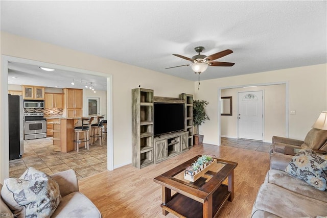 living room featuring a ceiling fan, a textured ceiling, and light wood-style floors