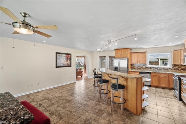 kitchen featuring ceiling fan, stainless steel appliances, baseboards, decorative backsplash, and a kitchen island
