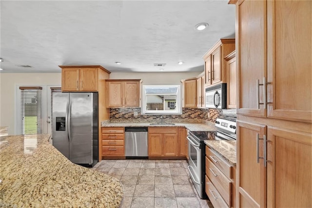 kitchen featuring backsplash, visible vents, a sink, light stone counters, and stainless steel appliances