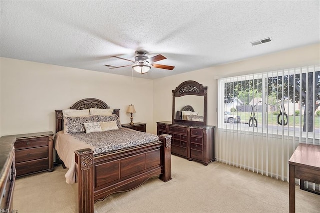 bedroom featuring a ceiling fan, a textured ceiling, visible vents, and light carpet