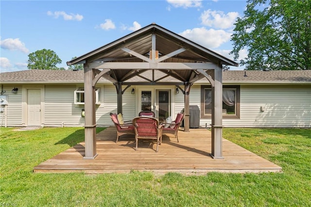 rear view of house featuring a lawn, a deck, and roof with shingles