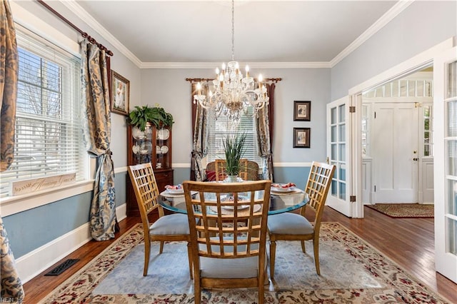 dining space featuring an inviting chandelier, ornamental molding, a wealth of natural light, and wood finished floors
