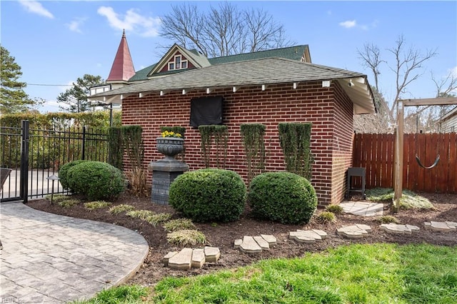 view of side of property with brick siding, a shingled roof, and fence