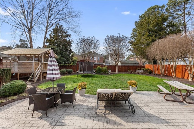 view of patio / terrace with outdoor dining area, a trampoline, a wooden deck, stairway, and a fenced backyard