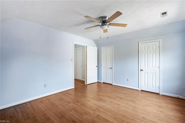 unfurnished bedroom featuring a ceiling fan, lofted ceiling, baseboards, visible vents, and light wood-style floors