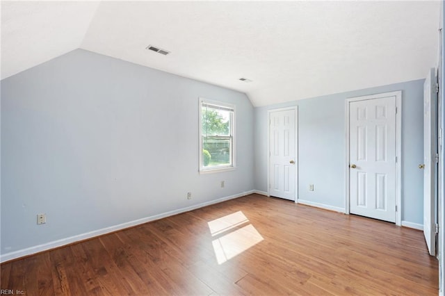 unfurnished bedroom with lofted ceiling, light wood-type flooring, visible vents, two closets, and baseboards