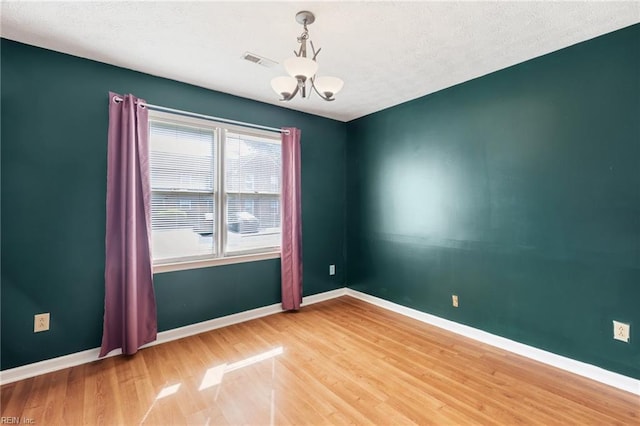 spare room with baseboards, a chandelier, visible vents, and wood finished floors