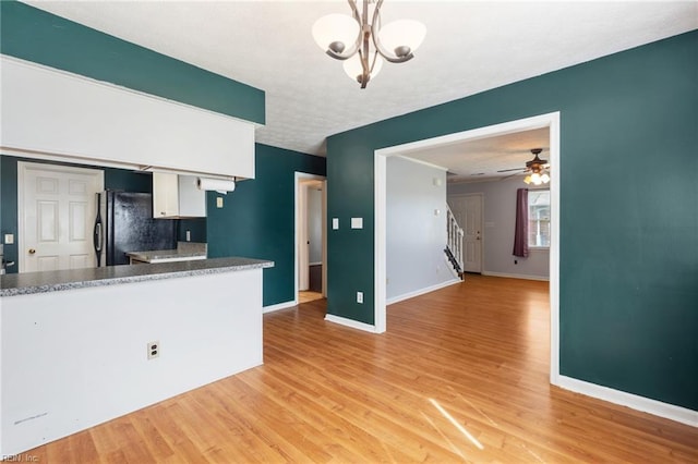 kitchen with freestanding refrigerator, baseboards, ceiling fan with notable chandelier, white cabinetry, and light wood-style floors