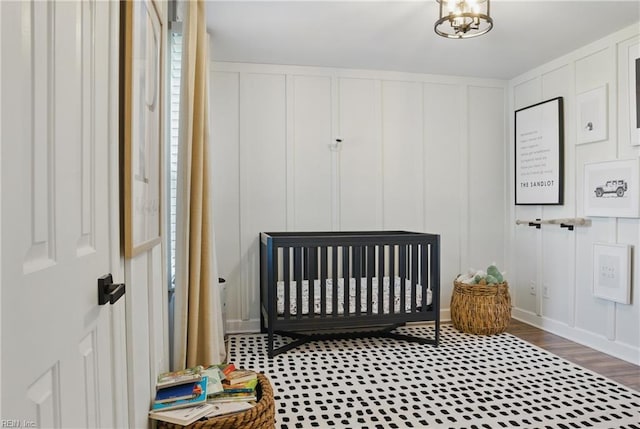 bedroom featuring a nursery area, wood finished floors, and a decorative wall
