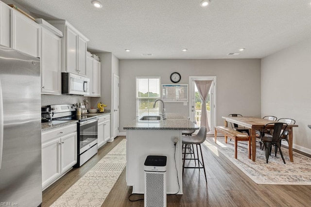 kitchen with a sink, appliances with stainless steel finishes, stone countertops, and wood finished floors