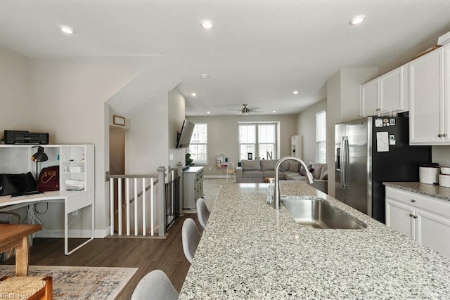 kitchen featuring white cabinets, dark wood-style flooring, light stone counters, a sink, and open floor plan