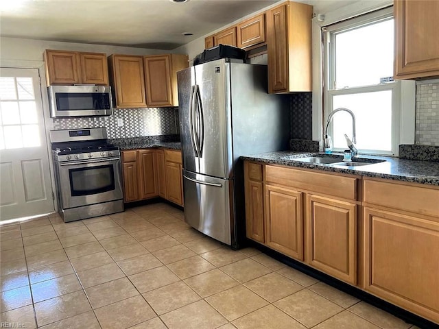 kitchen featuring tasteful backsplash, a sink, dark stone countertops, stainless steel appliances, and light tile patterned flooring