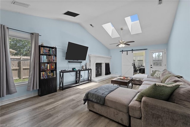 living room with a fireplace with raised hearth, a skylight, visible vents, and wood finished floors