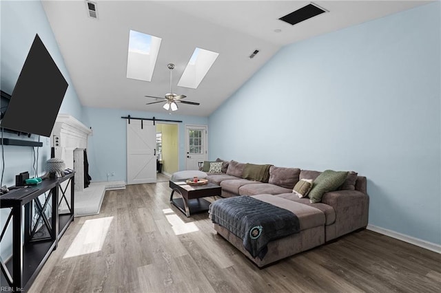 living room with visible vents, baseboards, light wood-type flooring, a barn door, and a skylight
