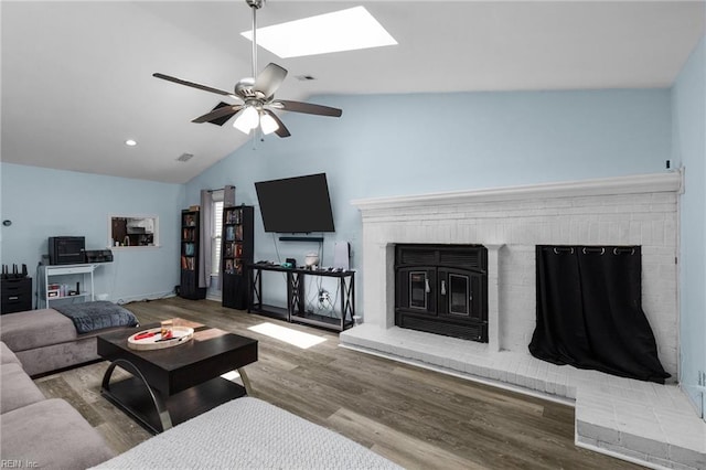 living room with vaulted ceiling with skylight, ceiling fan, a brick fireplace, wood finished floors, and recessed lighting