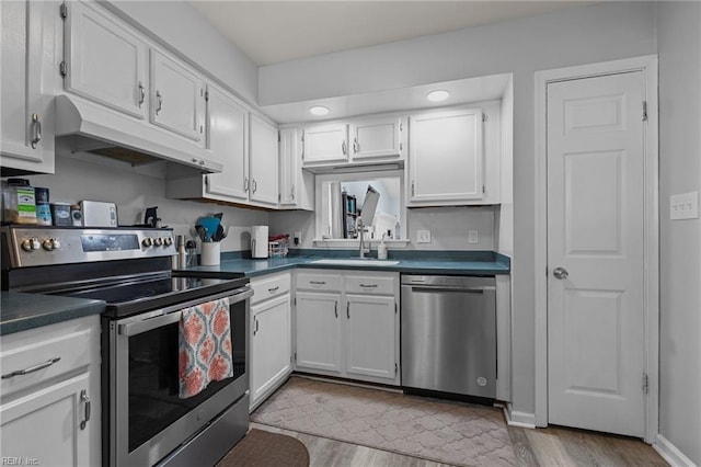 kitchen with dark countertops, under cabinet range hood, white cabinets, a sink, and appliances with stainless steel finishes
