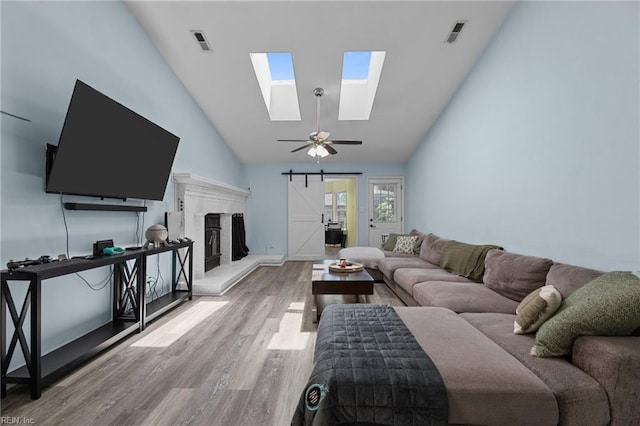 living area featuring visible vents, a skylight, a barn door, wood finished floors, and high vaulted ceiling