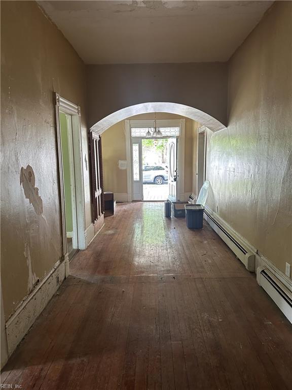 hallway with arched walkways, hardwood / wood-style flooring, and a baseboard radiator