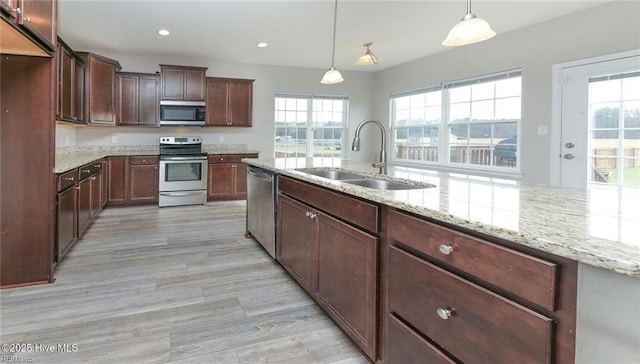 kitchen featuring stainless steel appliances, light stone counters, a sink, and light wood-style flooring