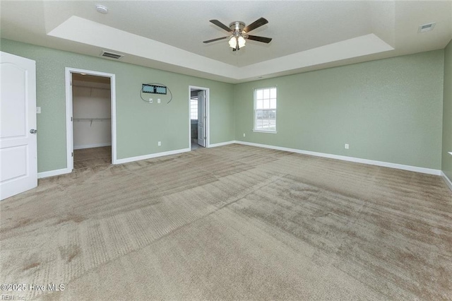 unfurnished bedroom with a raised ceiling, baseboards, a spacious closet, and visible vents