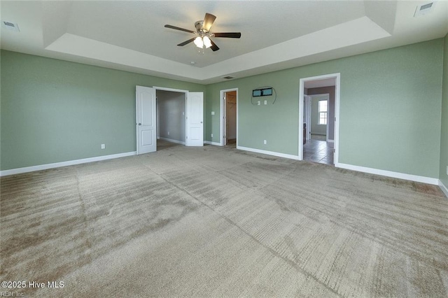 unfurnished bedroom featuring baseboards, a tray ceiling, a spacious closet, and light colored carpet