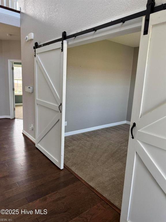 interior space featuring a textured ceiling, baseboards, a barn door, and wood finished floors