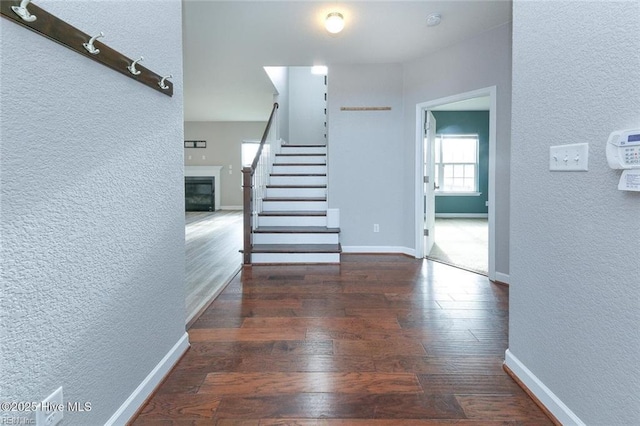 hall with baseboards, a textured wall, wood-type flooring, and stairs