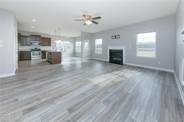 unfurnished living room featuring a ceiling fan, baseboards, a wealth of natural light, and light wood-type flooring