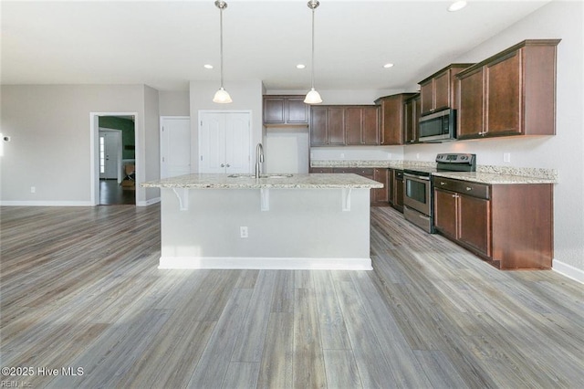 kitchen featuring a sink, light wood-style flooring, stainless steel appliances, baseboards, and a center island with sink