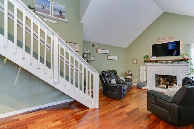 living area featuring visible vents, a fireplace, wood finished floors, stairway, and high vaulted ceiling