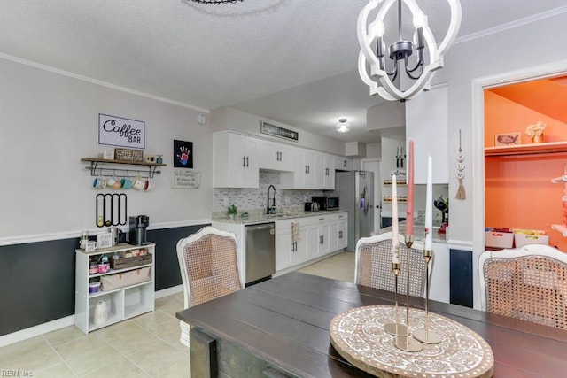 kitchen featuring appliances with stainless steel finishes, a sink, a chandelier, white cabinetry, and backsplash