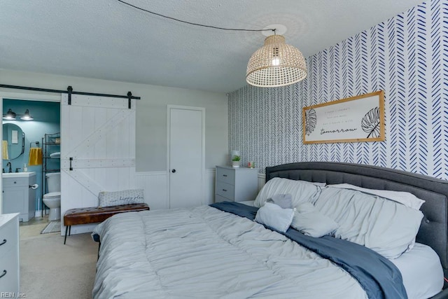 bedroom featuring light colored carpet, a barn door, a textured ceiling, a wainscoted wall, and wallpapered walls
