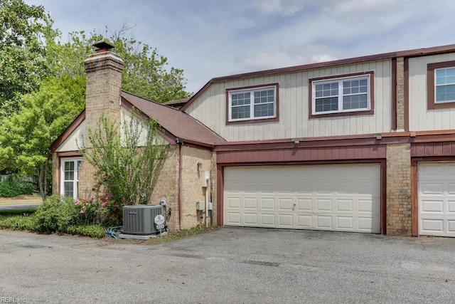 view of front of home featuring a chimney, brick siding, an attached garage, central air condition unit, and driveway