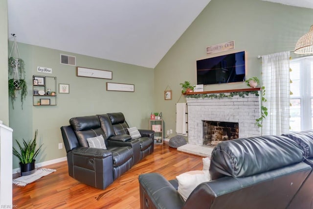 living area with a brick fireplace, high vaulted ceiling, baseboards, wood finished floors, and visible vents
