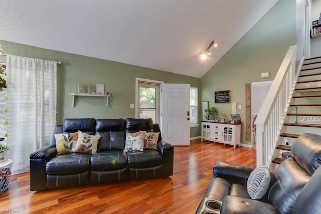 living room with stairway, high vaulted ceiling, wood finished floors, and track lighting