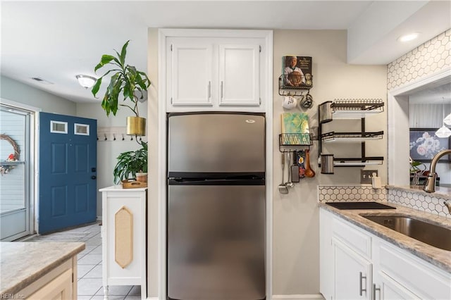 kitchen featuring decorative backsplash, visible vents, a sink, freestanding refrigerator, and white cabinetry
