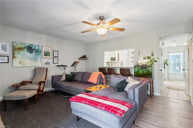 living room featuring baseboards, a ceiling fan, and light wood finished floors